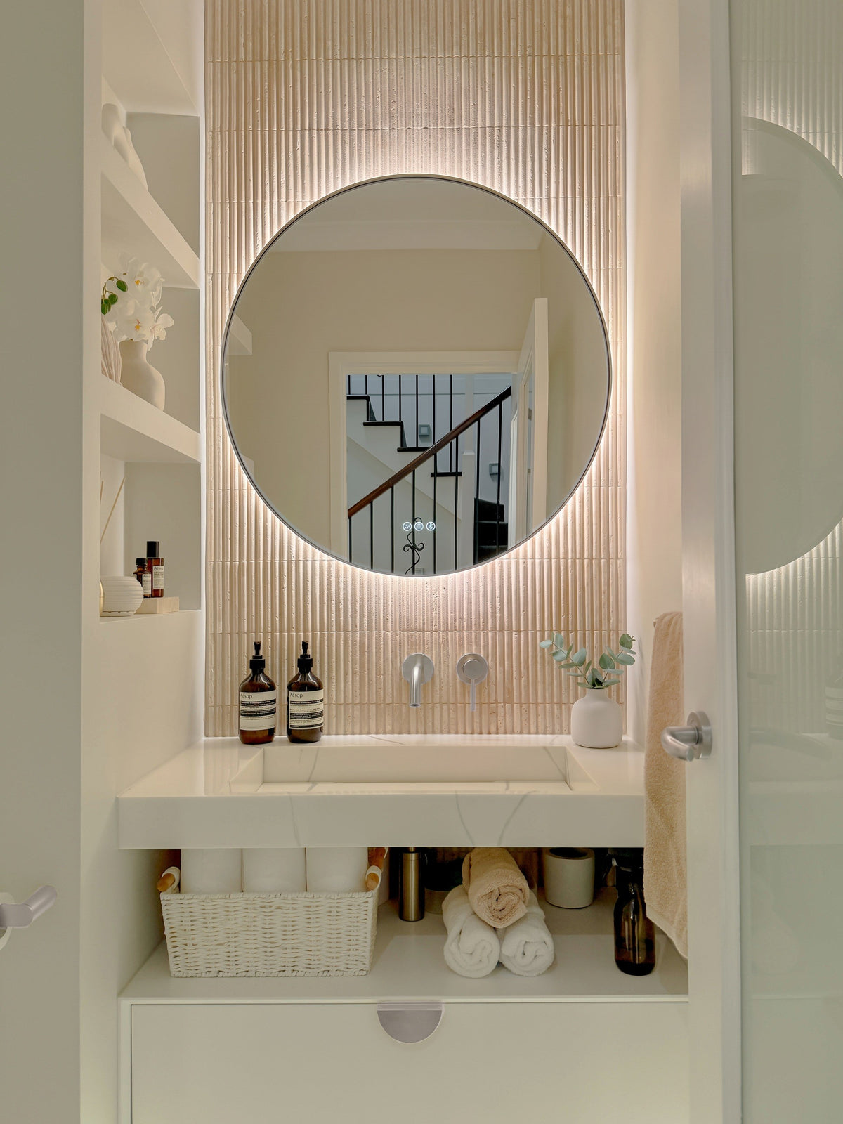 The Capri round 800 mm framed backlit LED mirror in Brushed Nickel, in a powder room above a floating white vanity with matching hardware