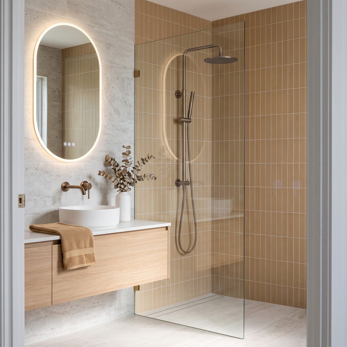 Corsica Dual Shower Head in Antique Brass, in a walk-in shower on tan tiles beside an oak vanity and pill mirror
