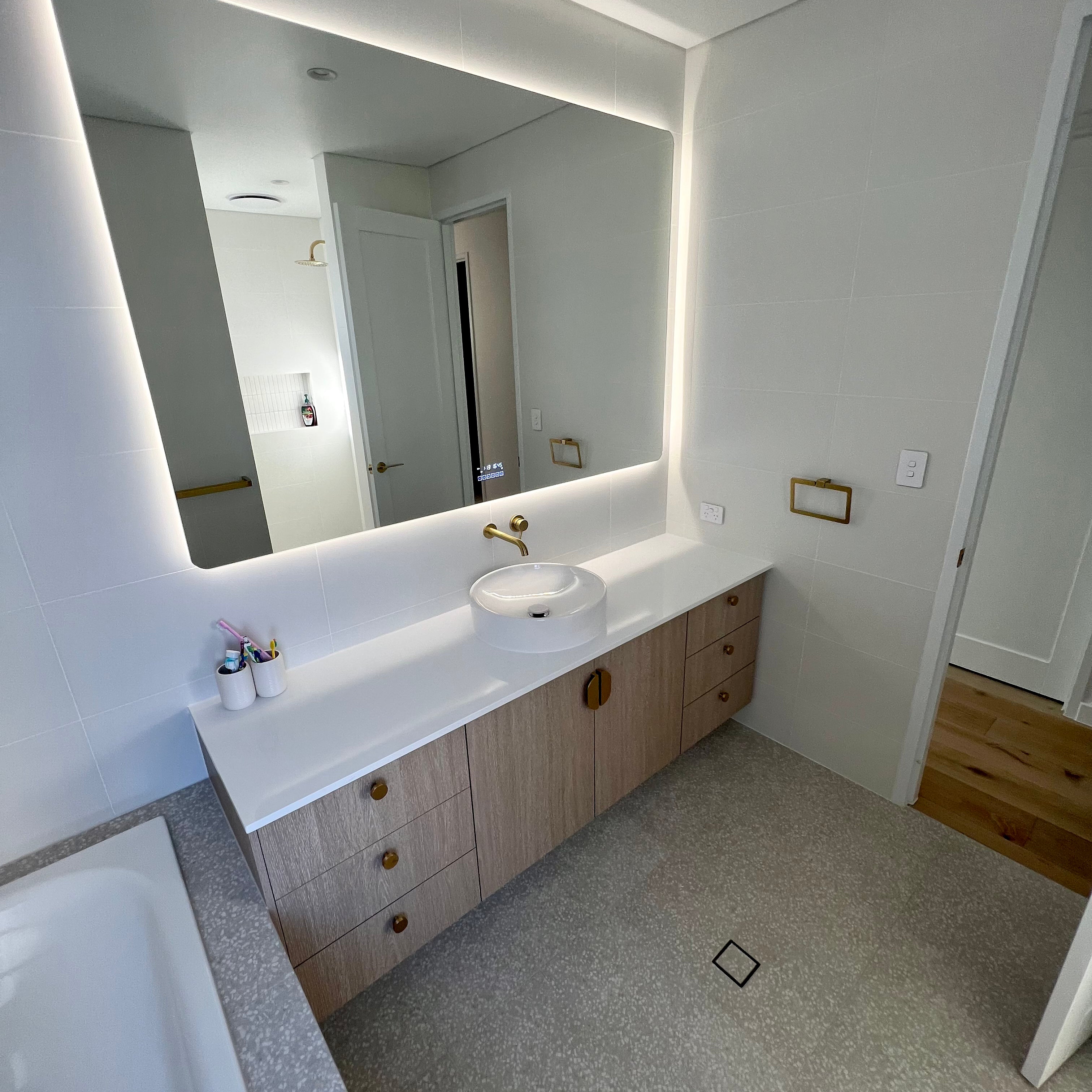 Corner View of White & Light Brown Themed Powder Room with Wall-to-Wall Smart LED Mirror