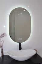 Oval Smart LED mirror above black countertop and white vessel sink