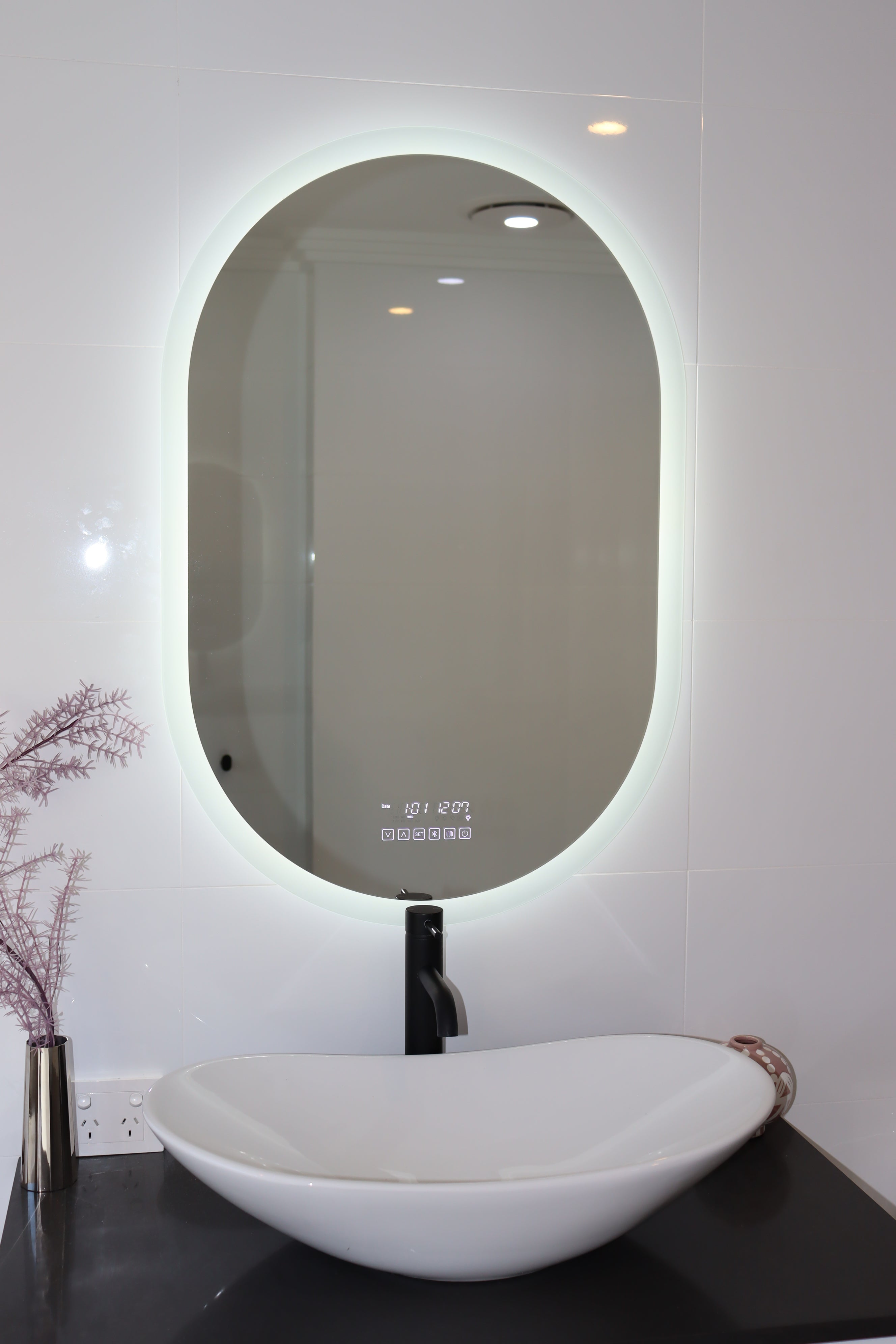 Oval Smart LED mirror above black countertop and white vessel sink