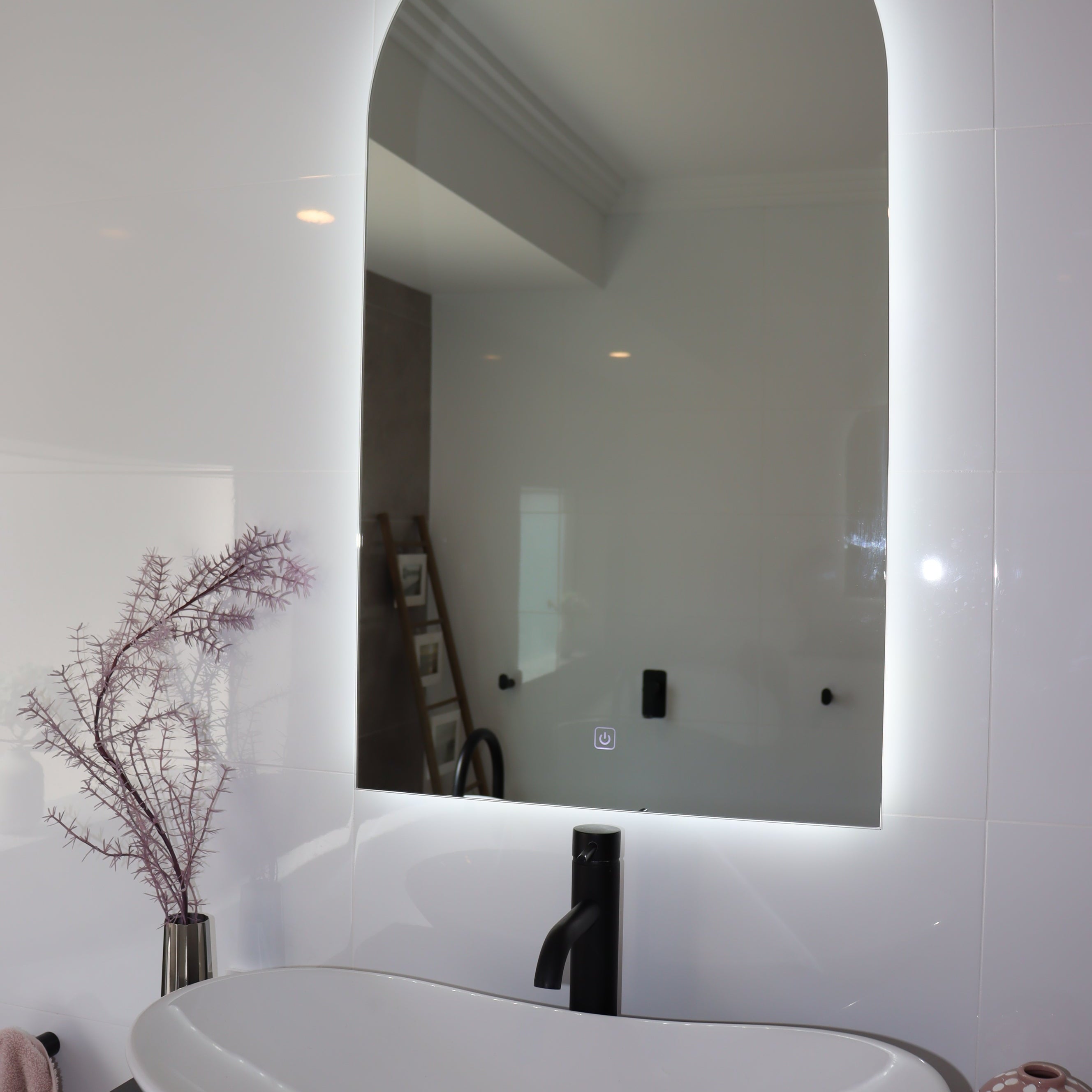 Curved Backlit LED mirror with White Vessel Sink, Black Countertop, and Faucet in White Bathroom