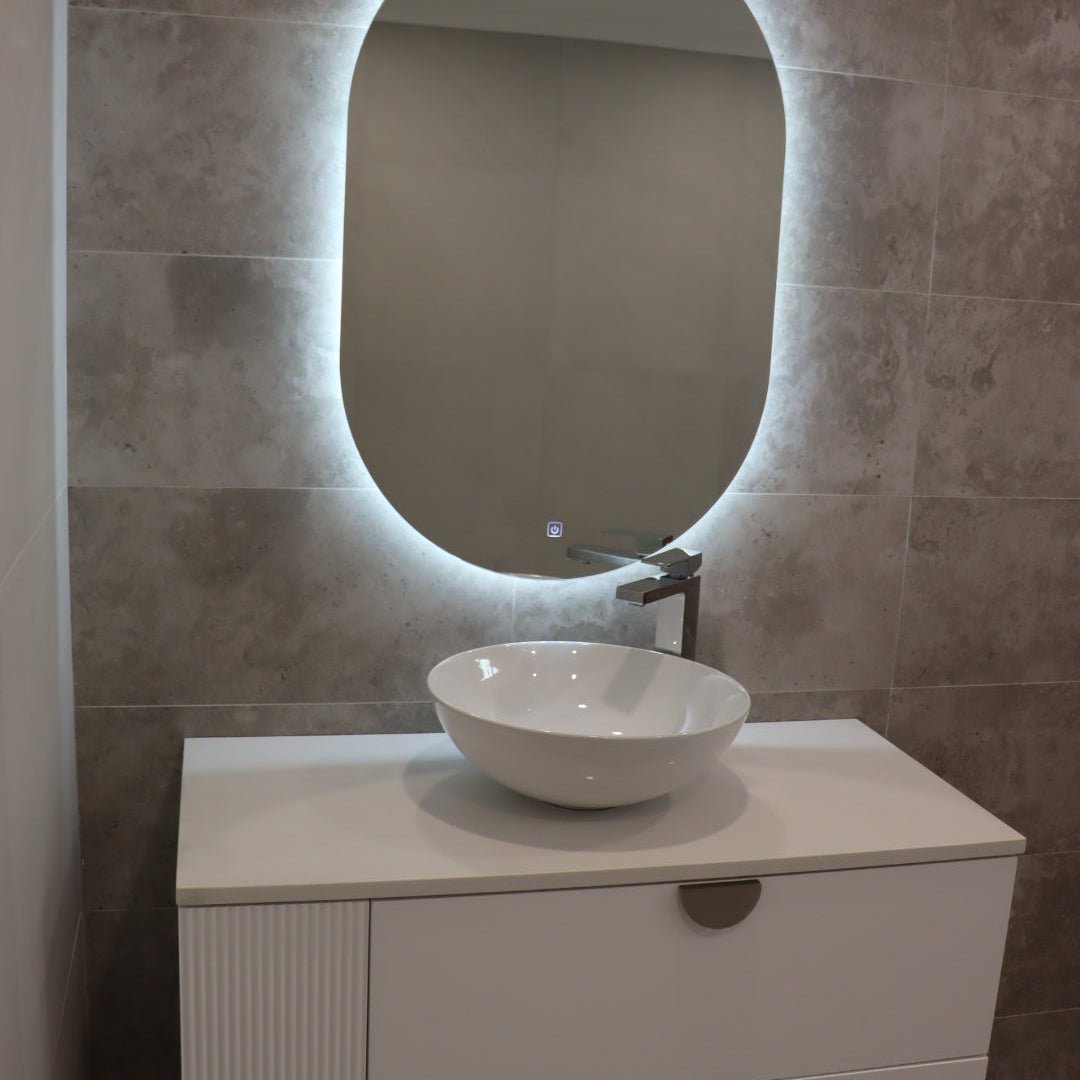 Left view of vanity space with Oval LED mirror emitting light, white floating cabinet with gold accents