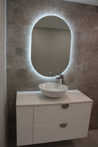 Left view of vanity space with Oval LED mirror emitting light, white floating cabinet with gold accents