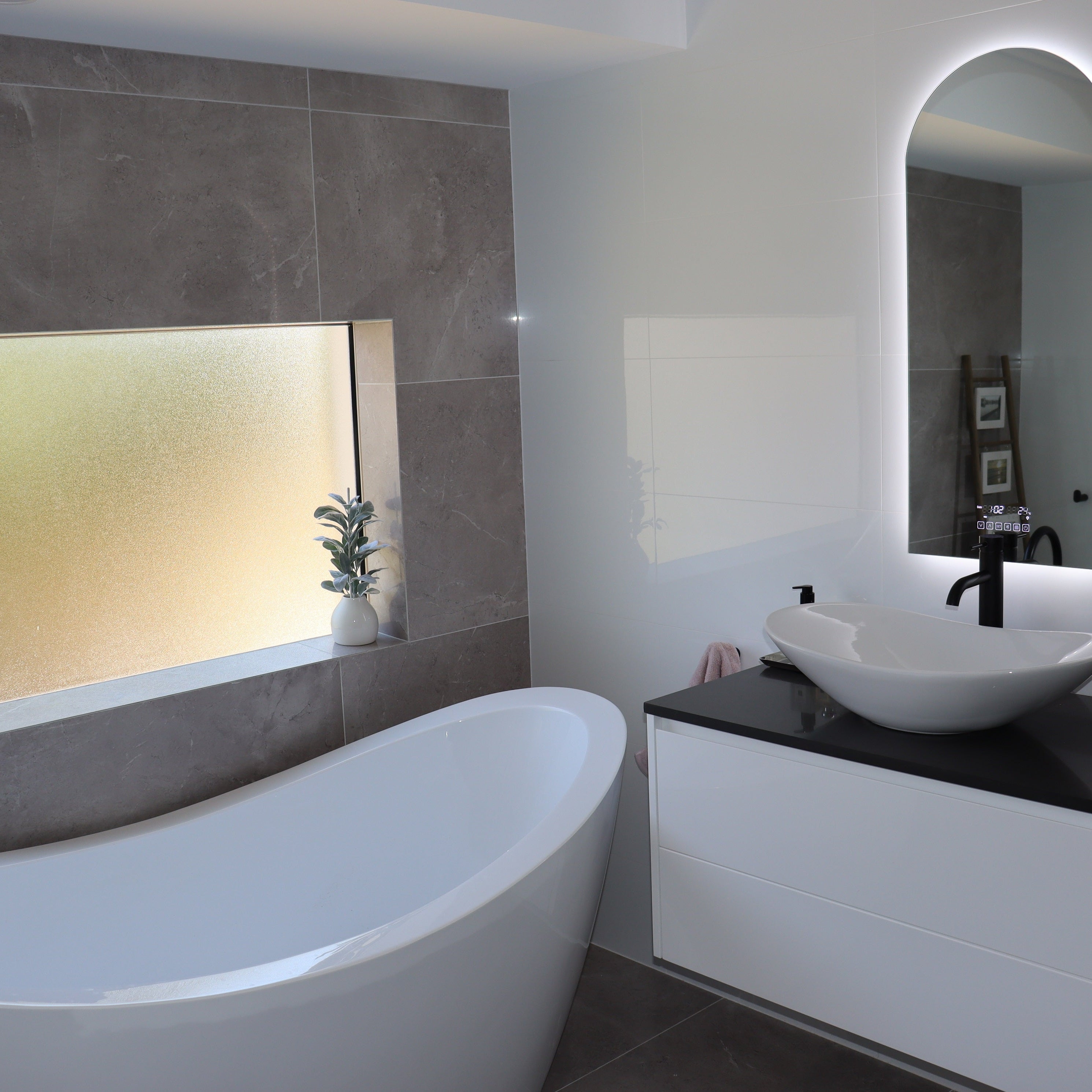 Backlit LED Mirror, White Vanity Cabinet and White Bathtub in White-Grey Bathroom with Black Accents