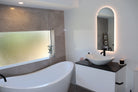 Split-design bathroom: Glossy white tiles, classy vanity, grey matte tiles, tinted window, bathtub.