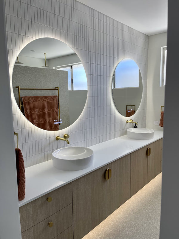 Round Smart LED Mirror on Vertical Stack Tile Wall in White and Brown Bathroom with Gold Accents