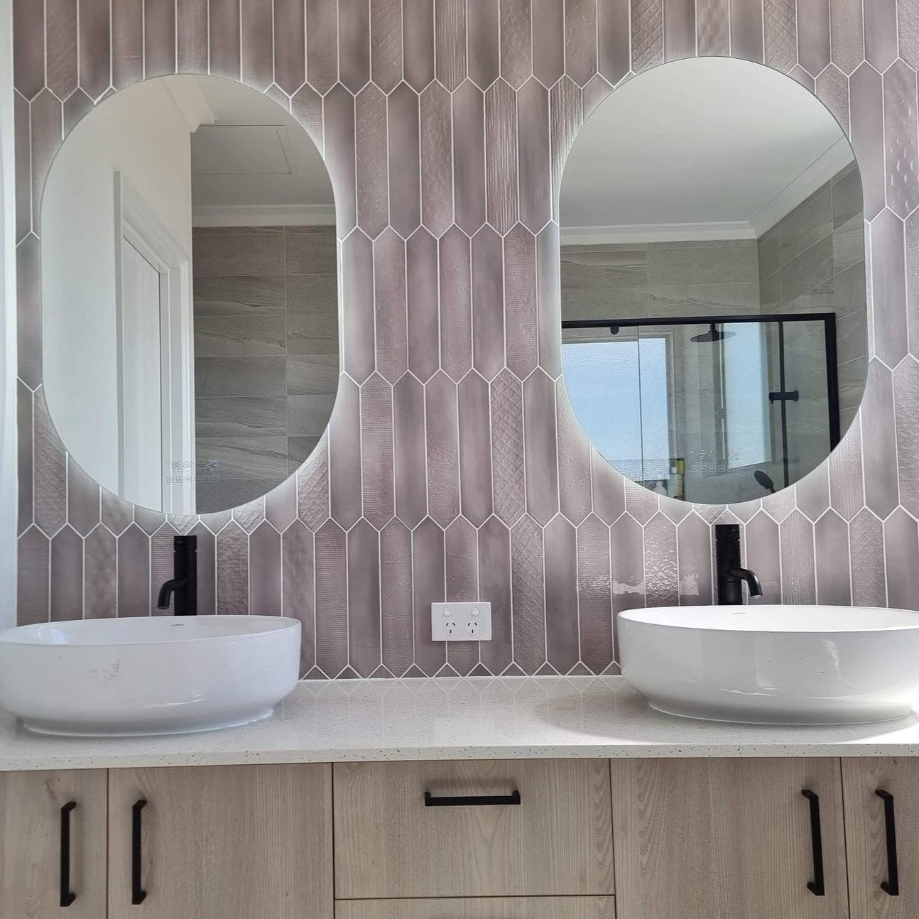 Pair of oval Smart LED mirrors and floating white and brown cabinet mounted on the picket-tiled wall