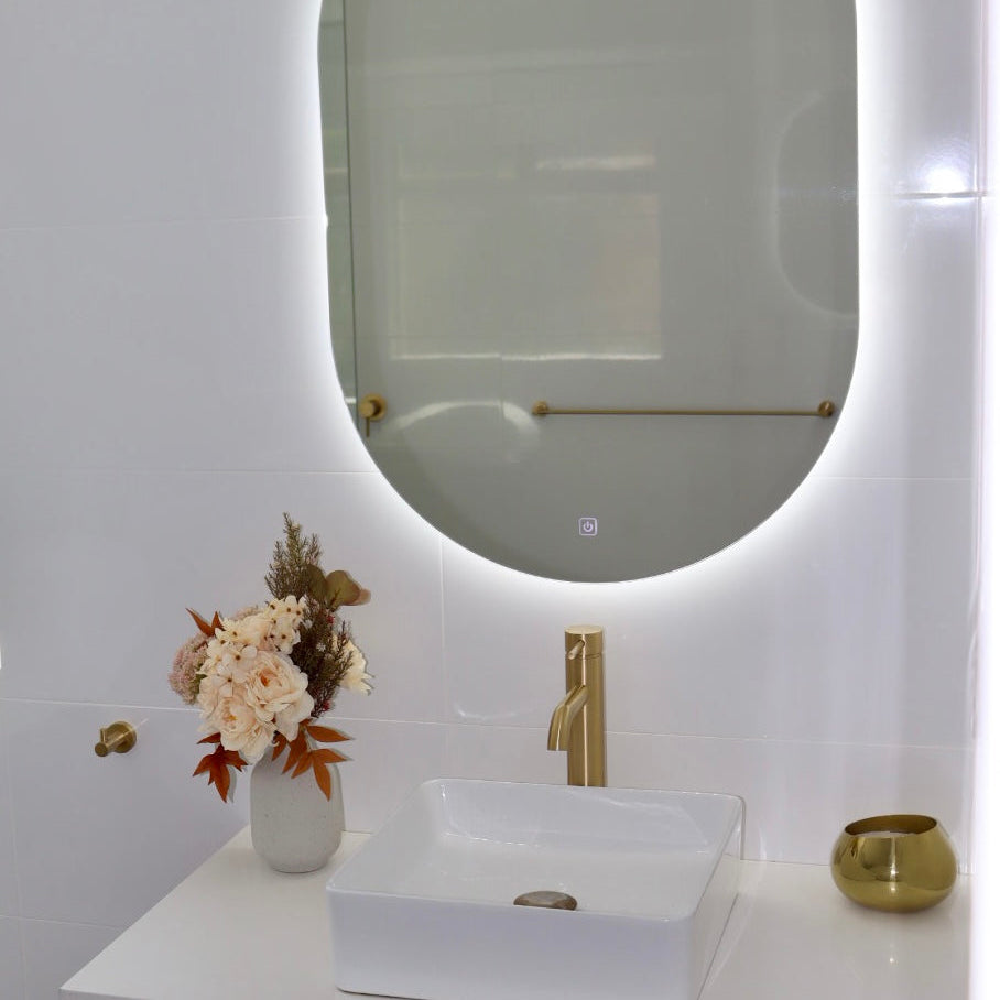 White-Lit LED Mirror Above White-Brown Floating Cabinet with Gold Accents on Shiny White Tiled Wall
