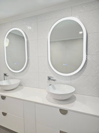 Doorway View of Two InVogue Mirrors' Silver Framed Oval Smart LED Mirrors in White-on-White Couple Bathroom
