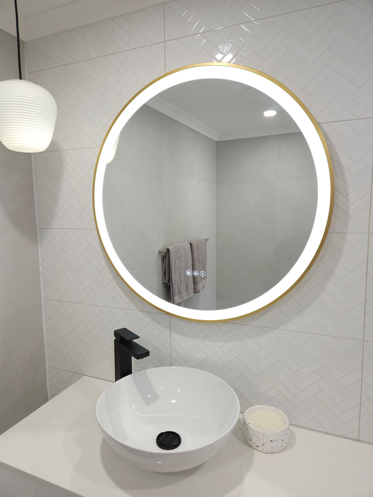 Circle-Shaped Smart LED Mirror in white-themed powder room with white sink, black faucet, hanging light & cabinet.