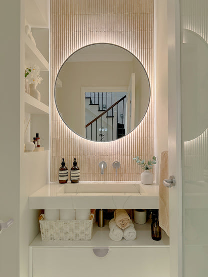 The Capri round 800 mm framed backlit LED mirror in Brushed Nickel, in a powder room above a floating white vanity with matching hardware