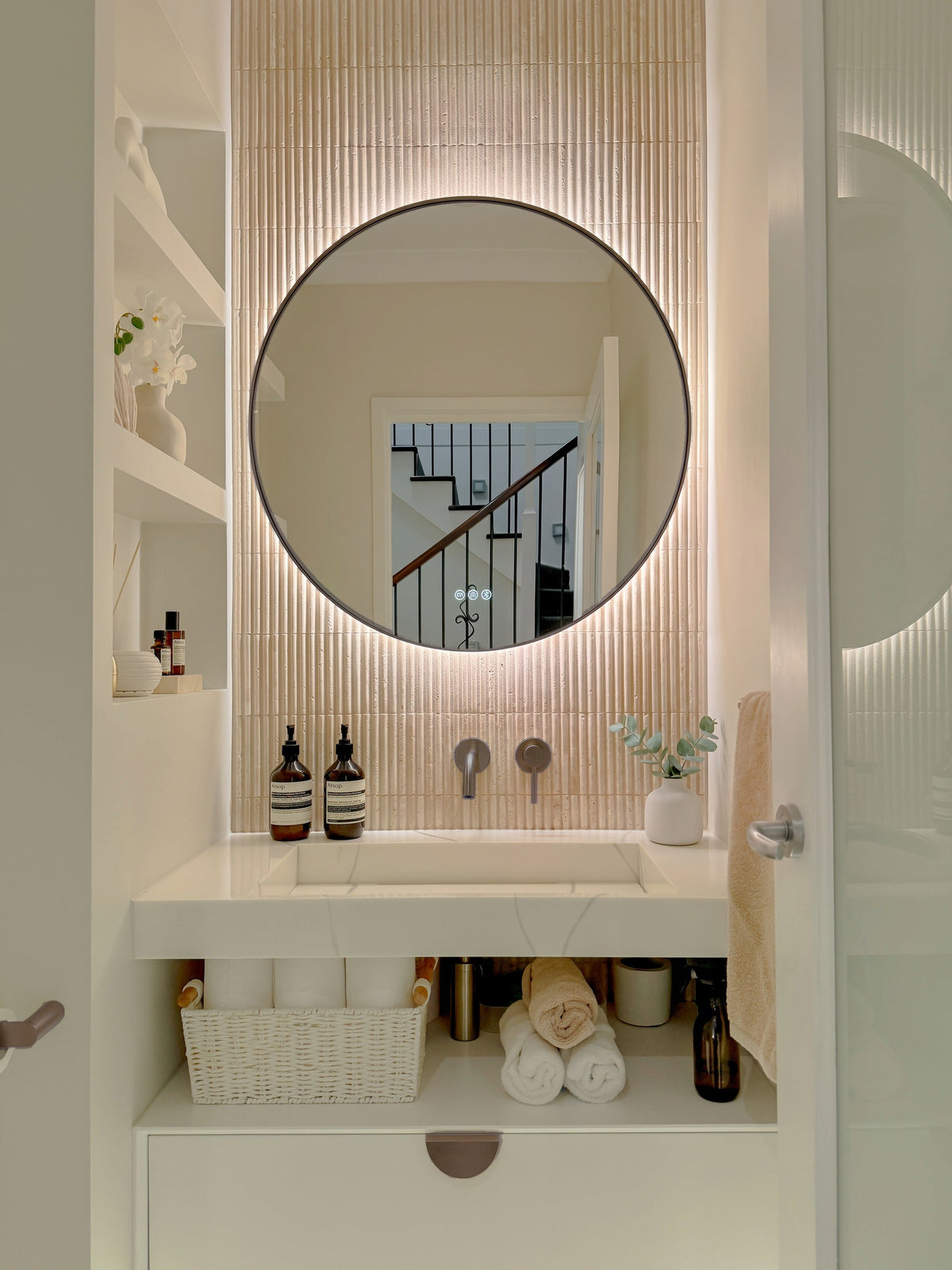 The Capri round 800 mm framed backlit LED mirror in Antique Brass, in a powder room above a floating white vanity with matching hardware