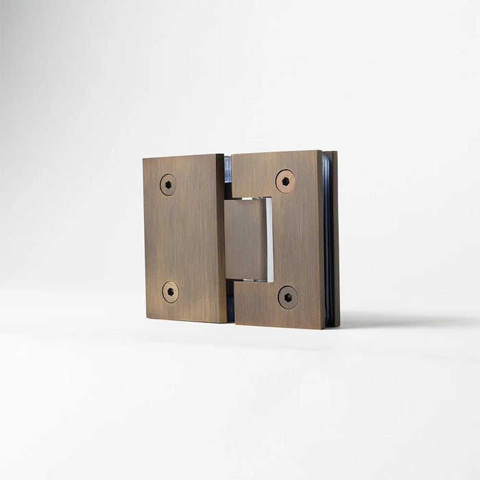 Geneva Shower Hinge Glass to Glass in Antique Brass, three-quarter view of the hinge standing on a plain white background