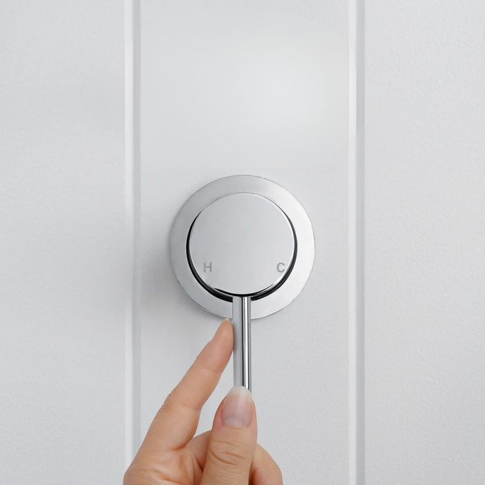 Milano Wall Mixer in Chrome, hand on the pin lever, front view on a white vertical-panelled wall