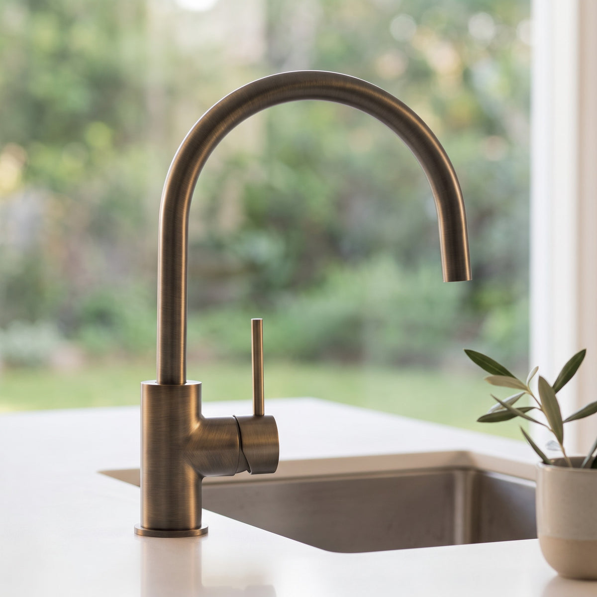 Como Kitchen Mixer Tap in Antique Brass, close view at a stainless sink beside a window with a garden view