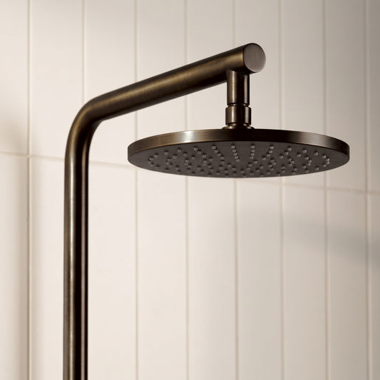 Corsica Dual Shower Head in Antique Brass, close-up of the round rain head and arm on white tiles