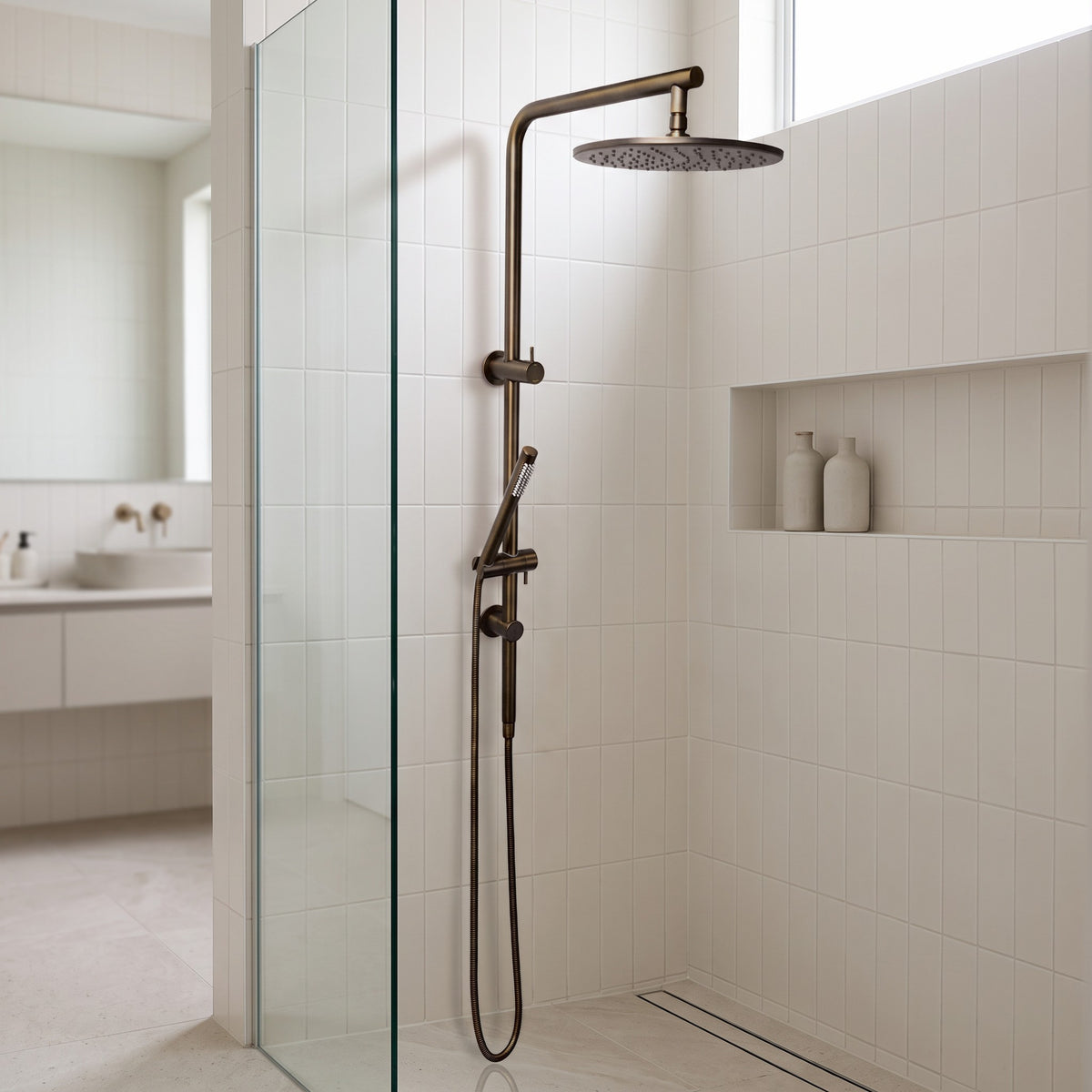 Corsica Dual Shower Head in Antique Brass, on warm-white stacked tiles in a walk-in shower with a niche