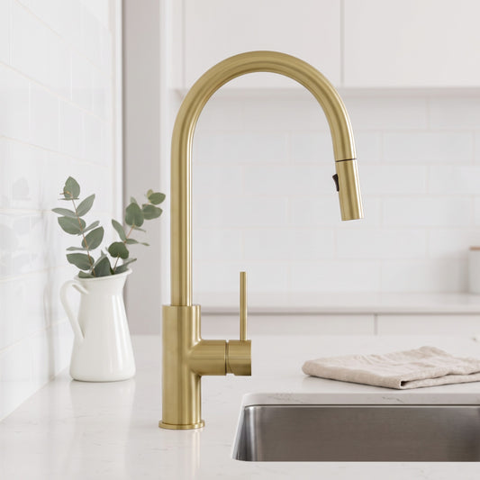 Porto Pull-Out Kitchen Mixer in Brushed Brass, at a stainless sink in a white kitchen beside a jug of eucalyptus