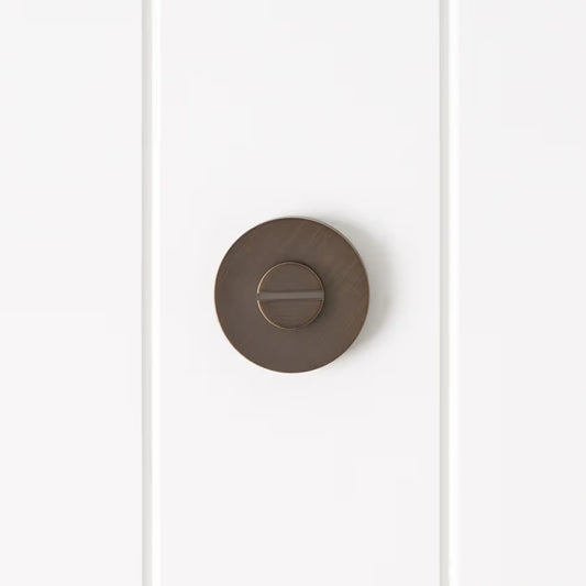 Prague Door Lock in Antique Brass, front view of the slotted emergency release on a white vertical-panelled wall