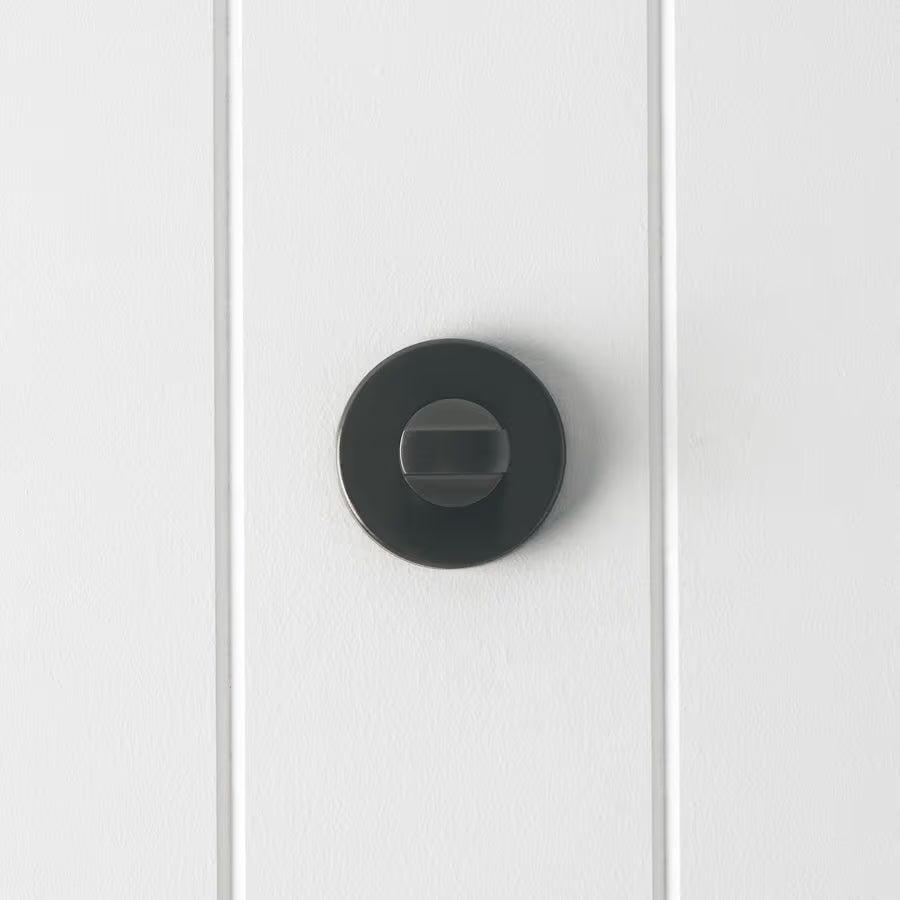 Prague Door Lock in Brushed Gunmetal, front view of the thumb-turn on its round rose, white vertical-panelled wall