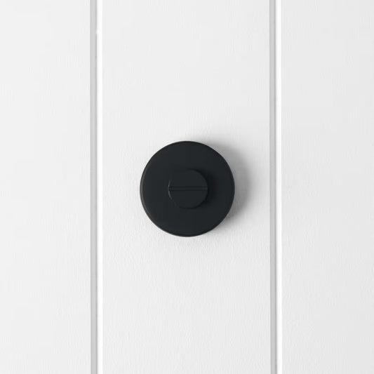 Prague Door Lock in Matte Black, front view of the slotted emergency release on a white vertical-panelled wall