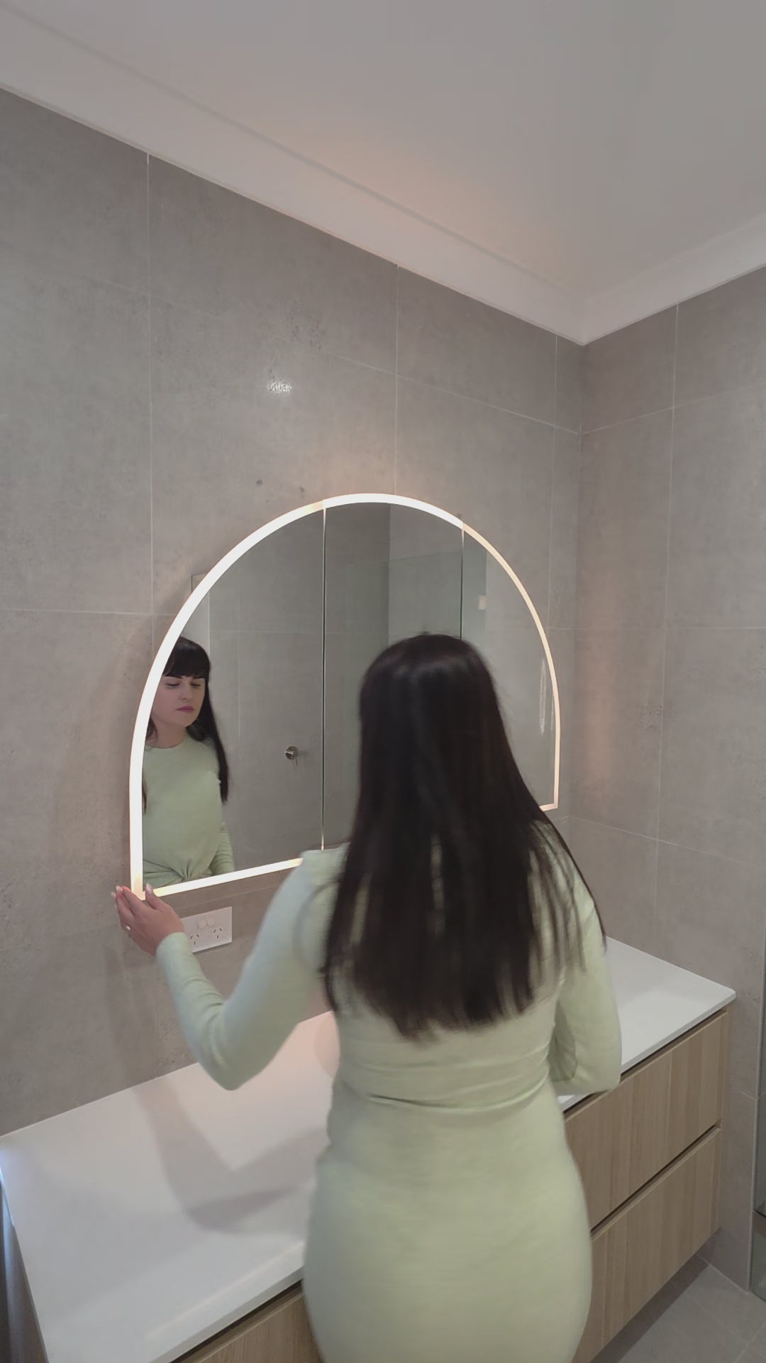 Female opening the door of an LED arched mirror cabinet showing adjustable glass internal shelves