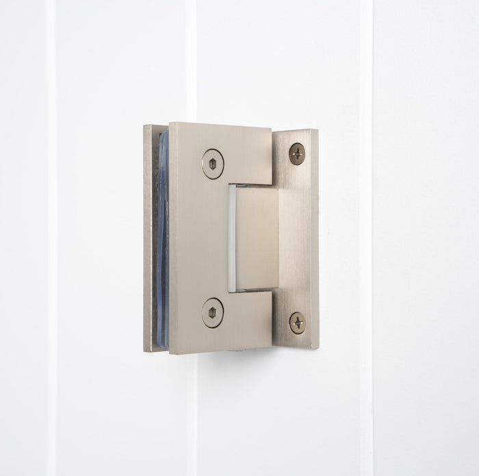 Rennes Shower Hinge Glass to Wall in Brushed Nickel, three-quarter view with clamped glass on a white vertical-panelled wall
