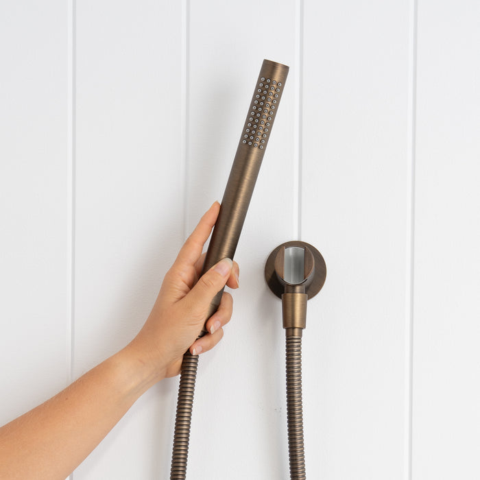 Versailles Handheld Shower Head with Hose in Antique Brass, hand holding the slim handpiece beside the round wall bracket