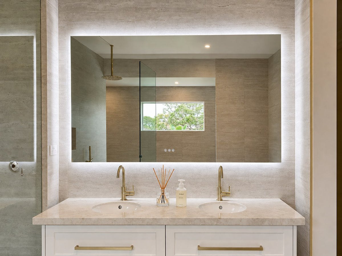 The Venice backlit LED bathroom mirror above a white double vanity with brass tapware and stone benchtop