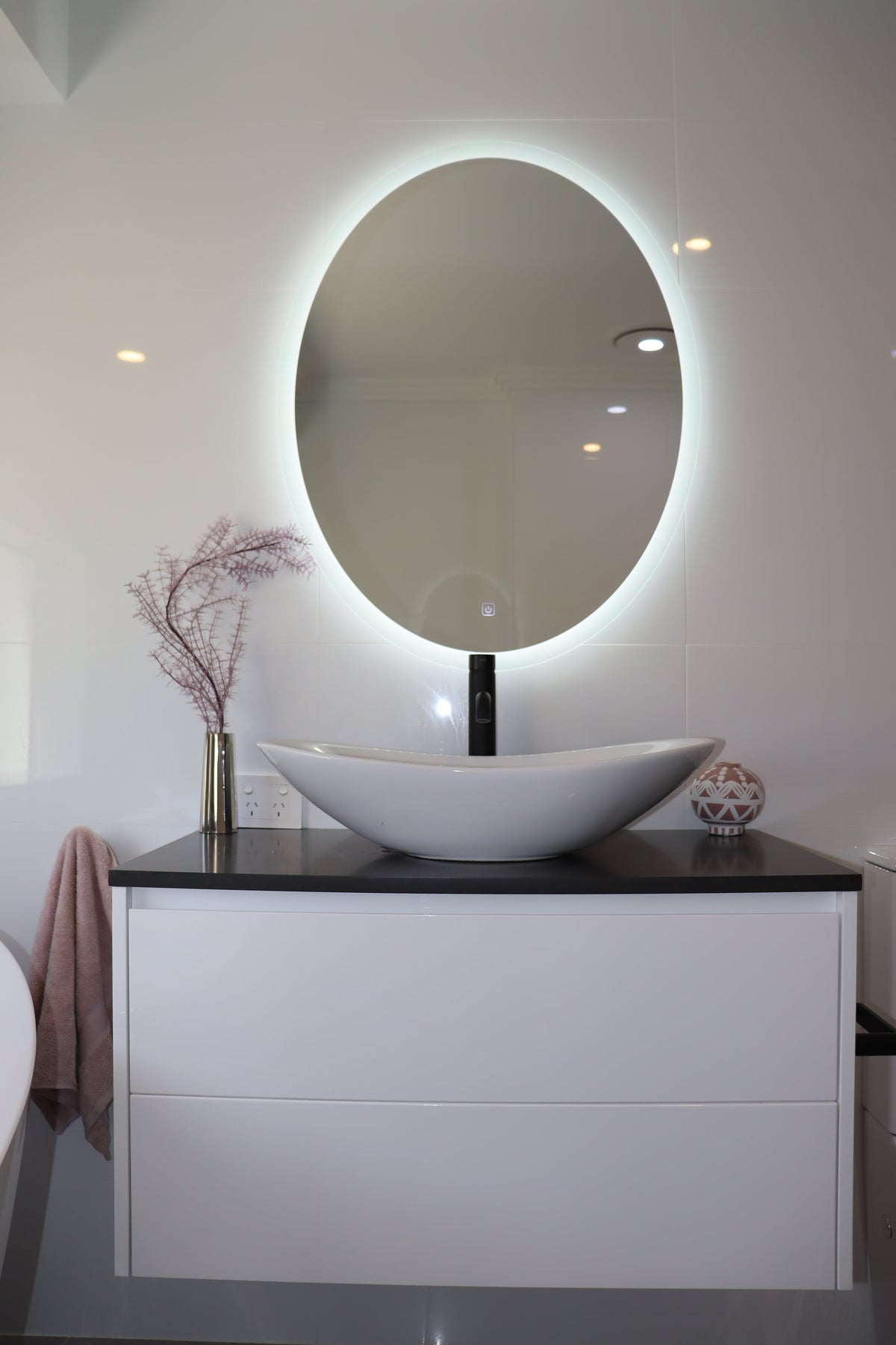 Soothing Light from Backlit Oval LED Mirror above Wall-Mounted Vanity Cabinet in White Bathroom