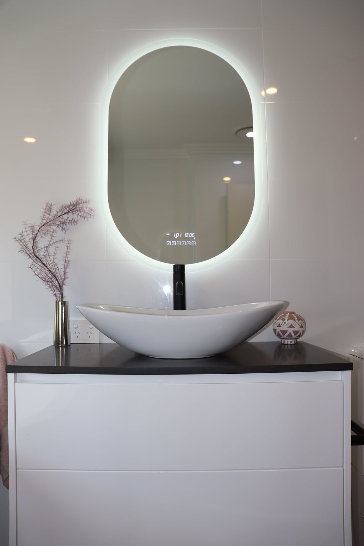 Pill-shaped Smart LED mirror radiating brilliant white backlit light in an all-white bathroom