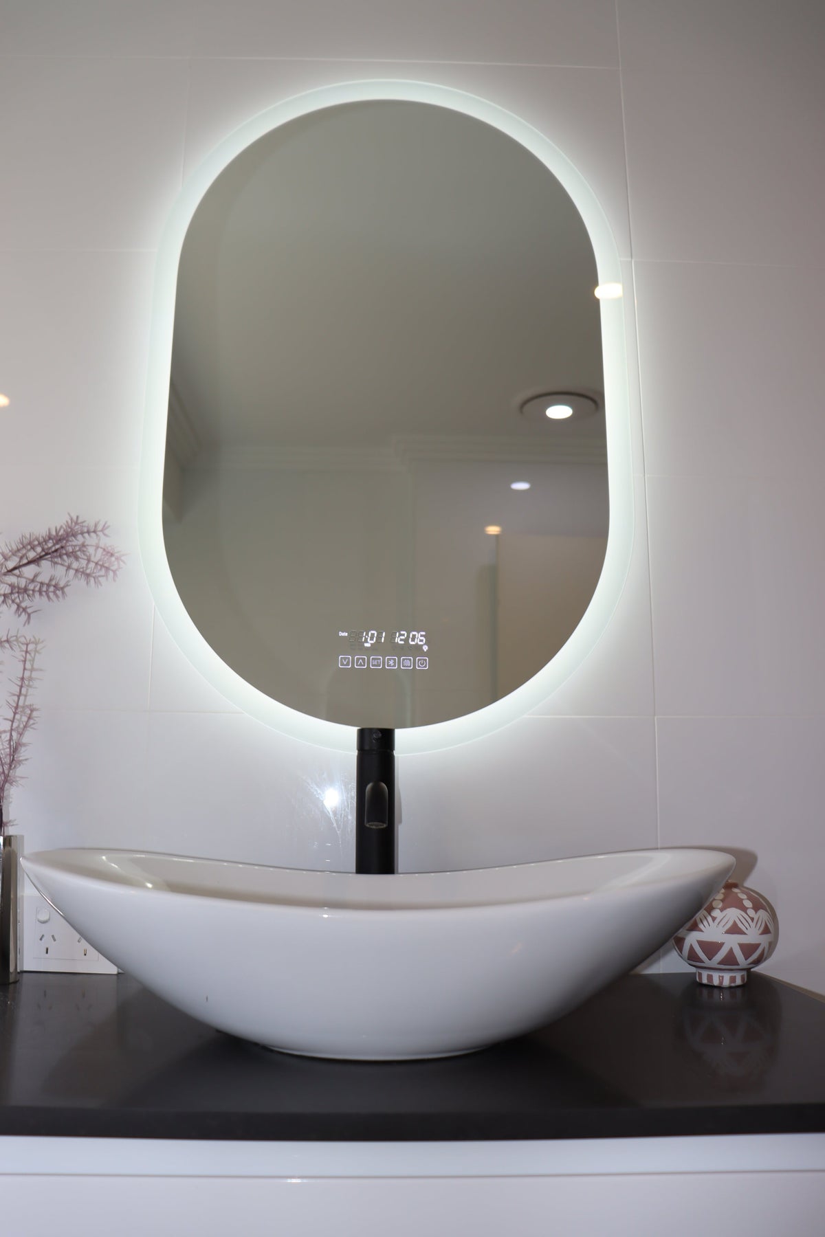 Oval Smart LED mirror emitting intense white backlit LED light, matched with white vessel sink below