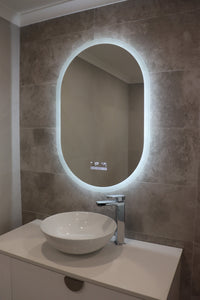 Vanity area with Smart LED mirror emitting brilliant white backlit light on greyish-brown tiled wall