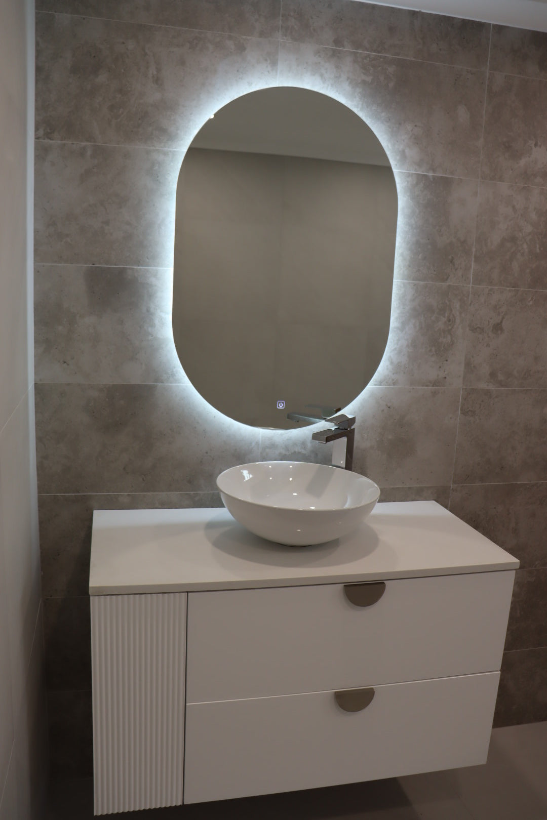 Left view of vanity space with Oval LED mirror emitting light, white floating cabinet with gold accents