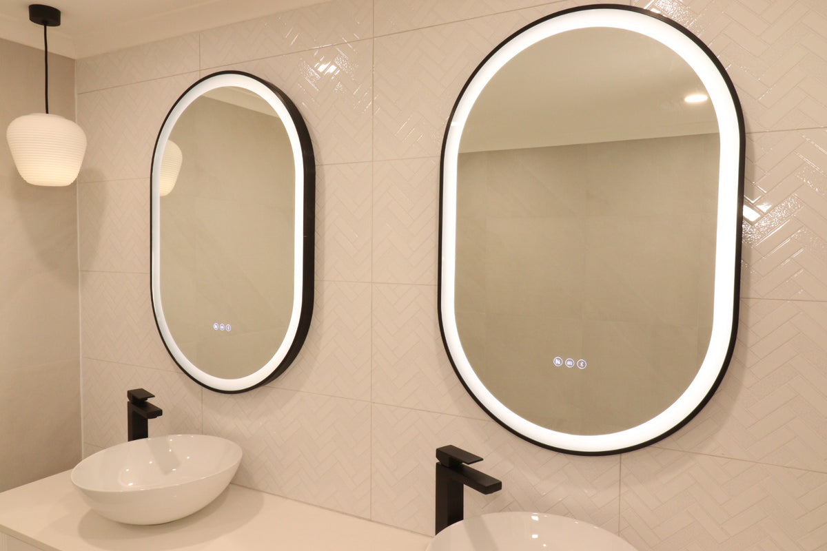 Right-side view of two InVogue Oval Black Frame Smart LED Vanity Mirrors in a cream-colored bathroom