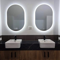 Oval LED Mirrors in Men's Washroom with Shiny White Wall and sink, and a Black Top Wooden Cabinet