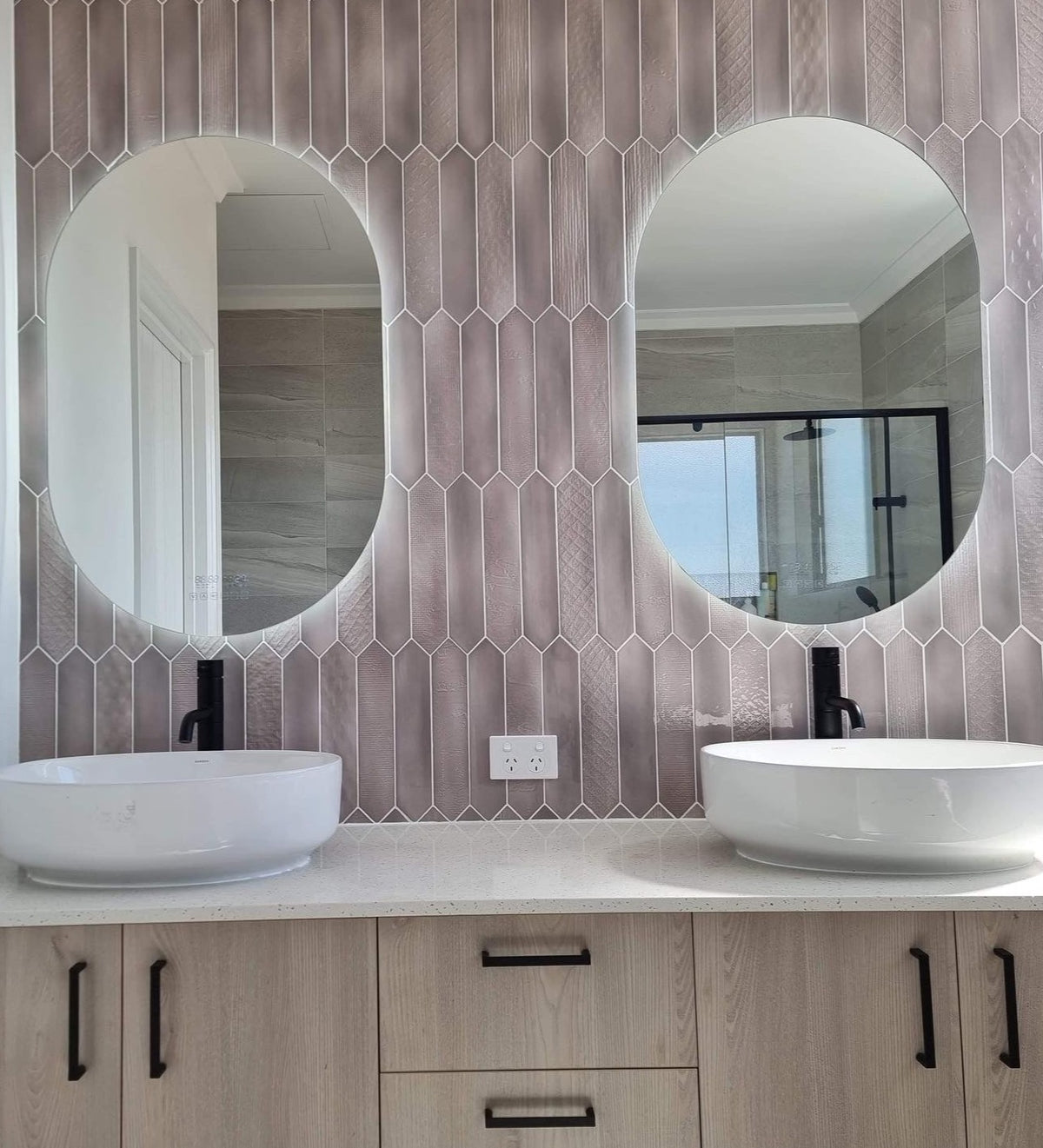 Pair of oval Smart LED mirrors and floating white and brown cabinet mounted on the picket-tiled wall