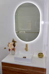 Compact Vanity Area with Oval LED Mirror Above Brown and White Cabinet in Shiny White Tiled Bathroom