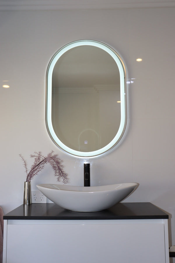 Oval LED Mirror and White Vanity Cabinet with Black Countertop and Sink in a Modern White Bathroom