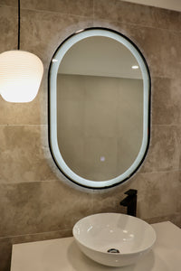 Left View of Oval Black Frame LED Mirror Above White Vessel Sink and Pendant Light